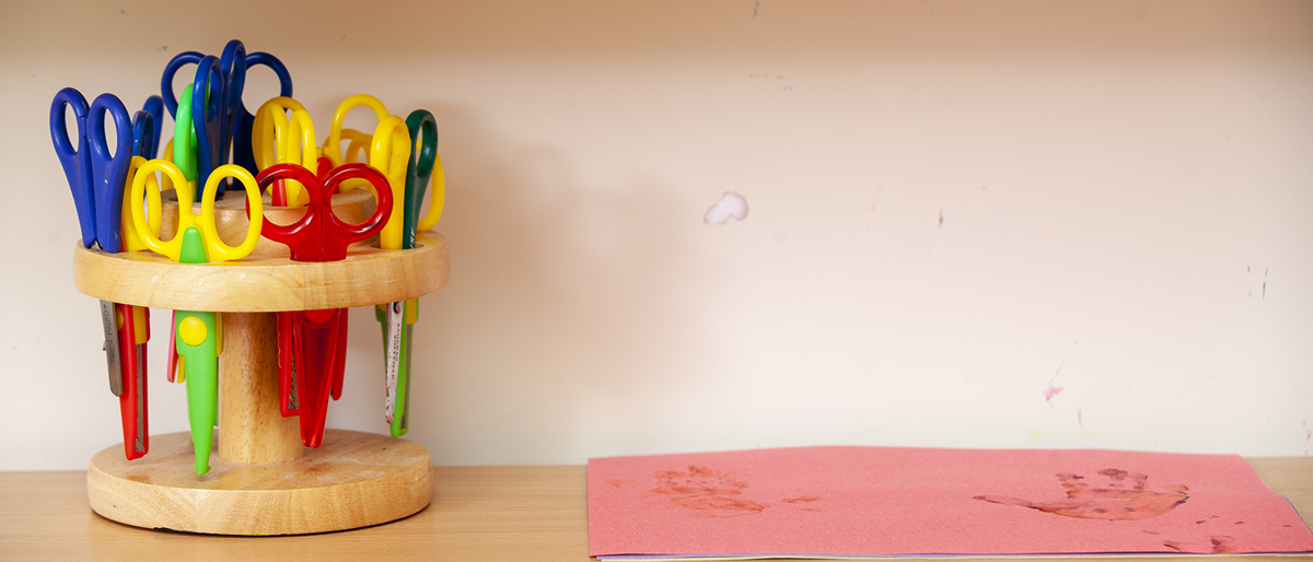 coloured scissors in a scissor rack on a shelf with paper next to them
