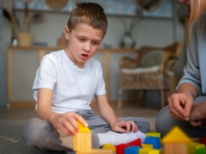 Mum sitting on the floor with son whilst he plays with toy blocks