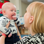 Mother holding her baby up to her face and smiling. The baby has their mouth wide open with their fist near their mouth.