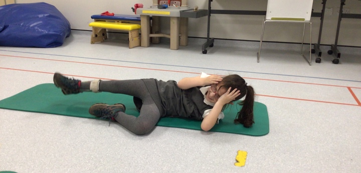 Child on yoga mat rolls onto their side, keeping their hands on their head