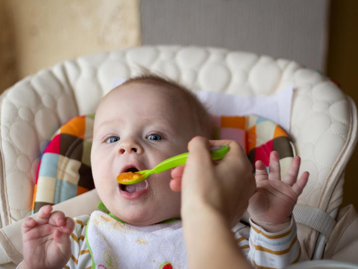 Baby boy sitting in a highchair being fed food from a spoon