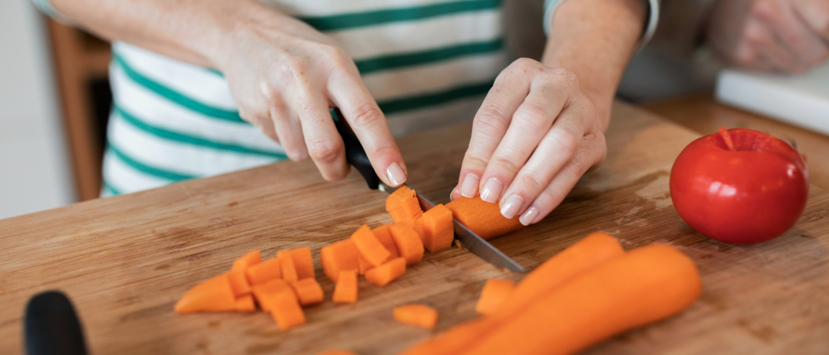 Woman in a stripey jumper chopping a carrot on a chopping board