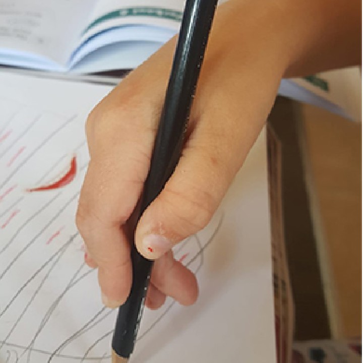 Child demonstrating the digital pronate grasp with a pencil and drawing on a piece of paper