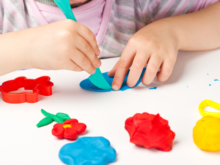 Child playing with colourful playdough on a table.