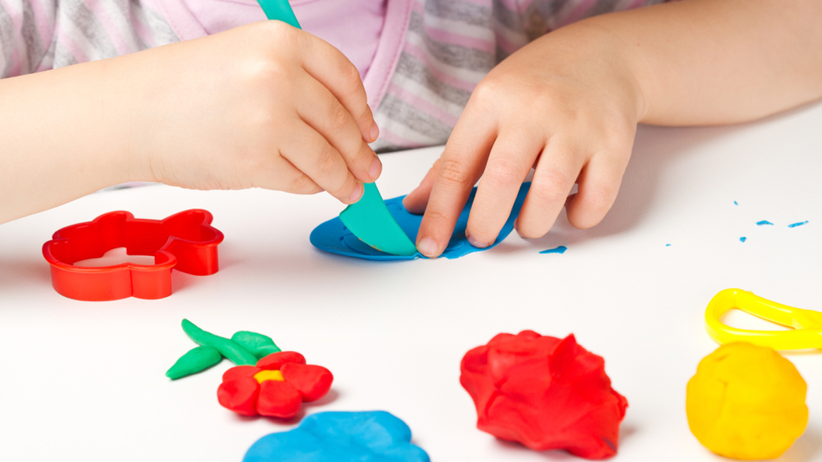Child playing with colourful playdough on a table.