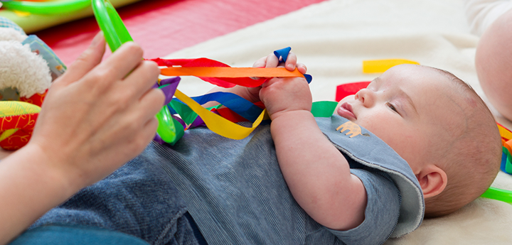 Baby lying on their back on a mat playing with a multi-coloured string toy