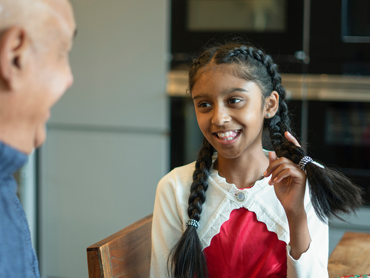 Girl sitting down fiddling with her hair and smiling. She is facing a man who is smiling back at her.