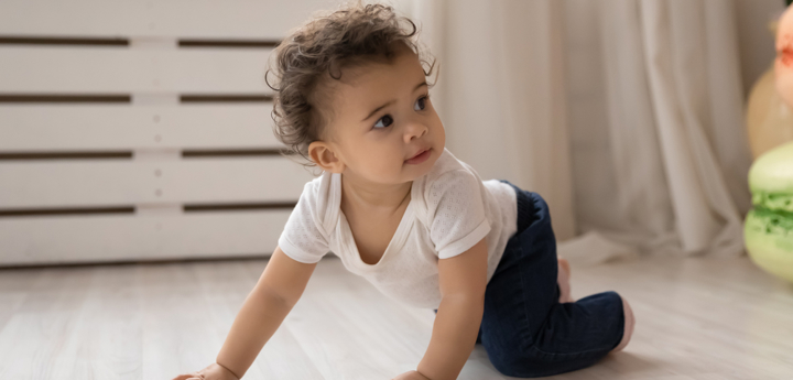 Baby crawling on their hands and knees across the floor.