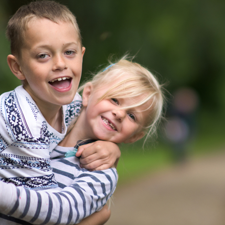 A young boy and young girl wrapping their arms round each other and smiling towards the camera.