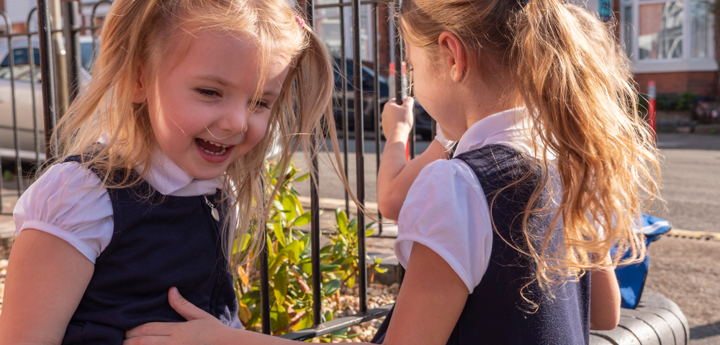 Two young primary school girls laughing together in the playground.