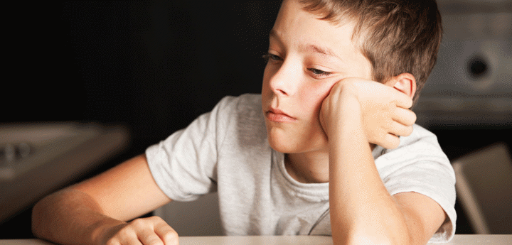 boy sat at table with head resting against hand looking bored