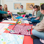 A group of 6 women sitting together on the floor with their babies lying on a playmat in front of them