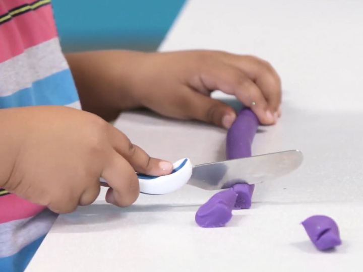 Young boy holding a knife cutting some playdough into pieces.