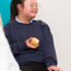 Girl with down syndrome sitting on a chair dressed in school uniform. She is smiling whilst talking and holding an apple.
