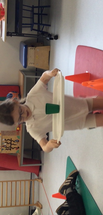 Child carrying a tray with a glass ull of water walks on her knees around some cones on the floor