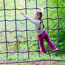 Young girl climbing on a rope net climbing frame in a woodland adventure playground. 