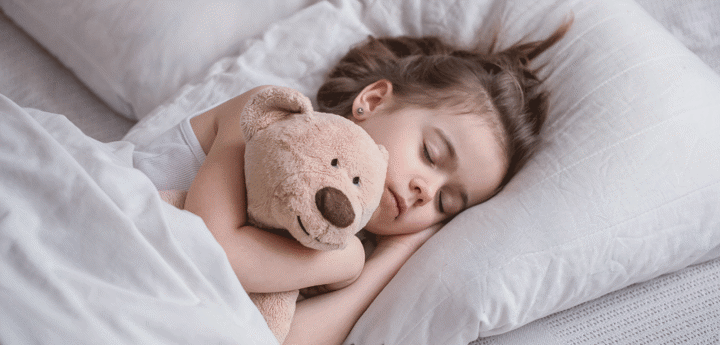 Little girl in bed sleeping cuddling a teddy bear