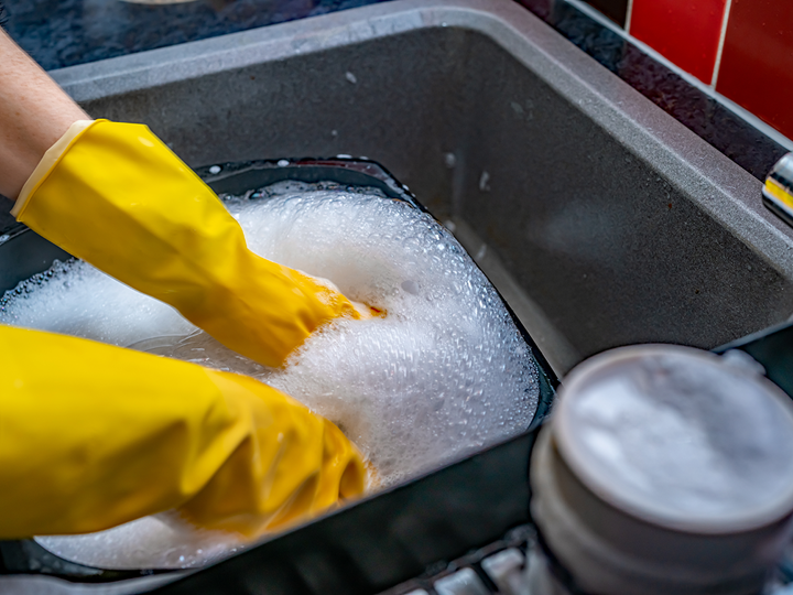 Washing up dishes in a sink with yellow gloves