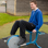 Teenage boy in school uniform sitting on exercise equipment outside.