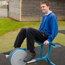 Teenage boy in school uniform sitting on exercise equipment outside.