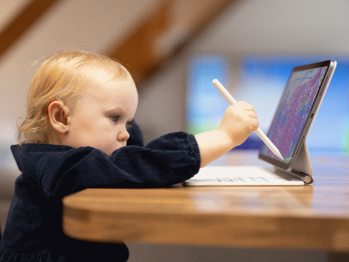 Toddler girl drawing on digital tablet at home whilst sitting at a table
