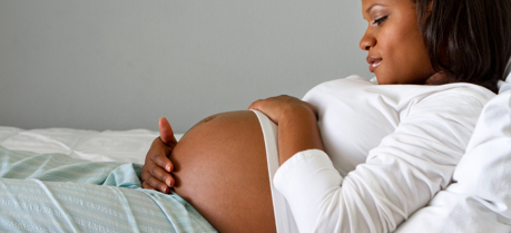 Pregnant woman lying on bed holding her stomach