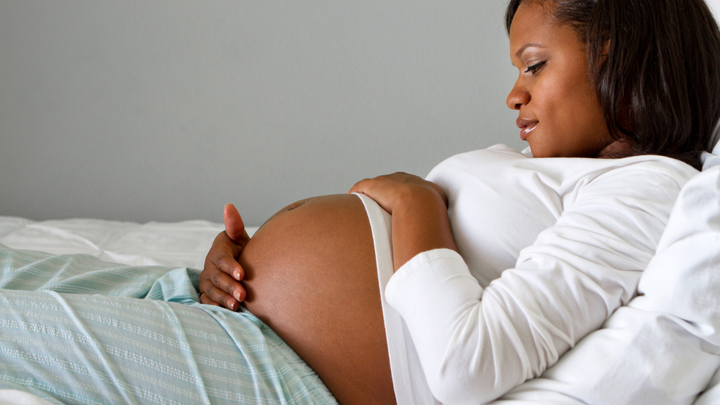 Pregnant woman lying on bed holding her stomach