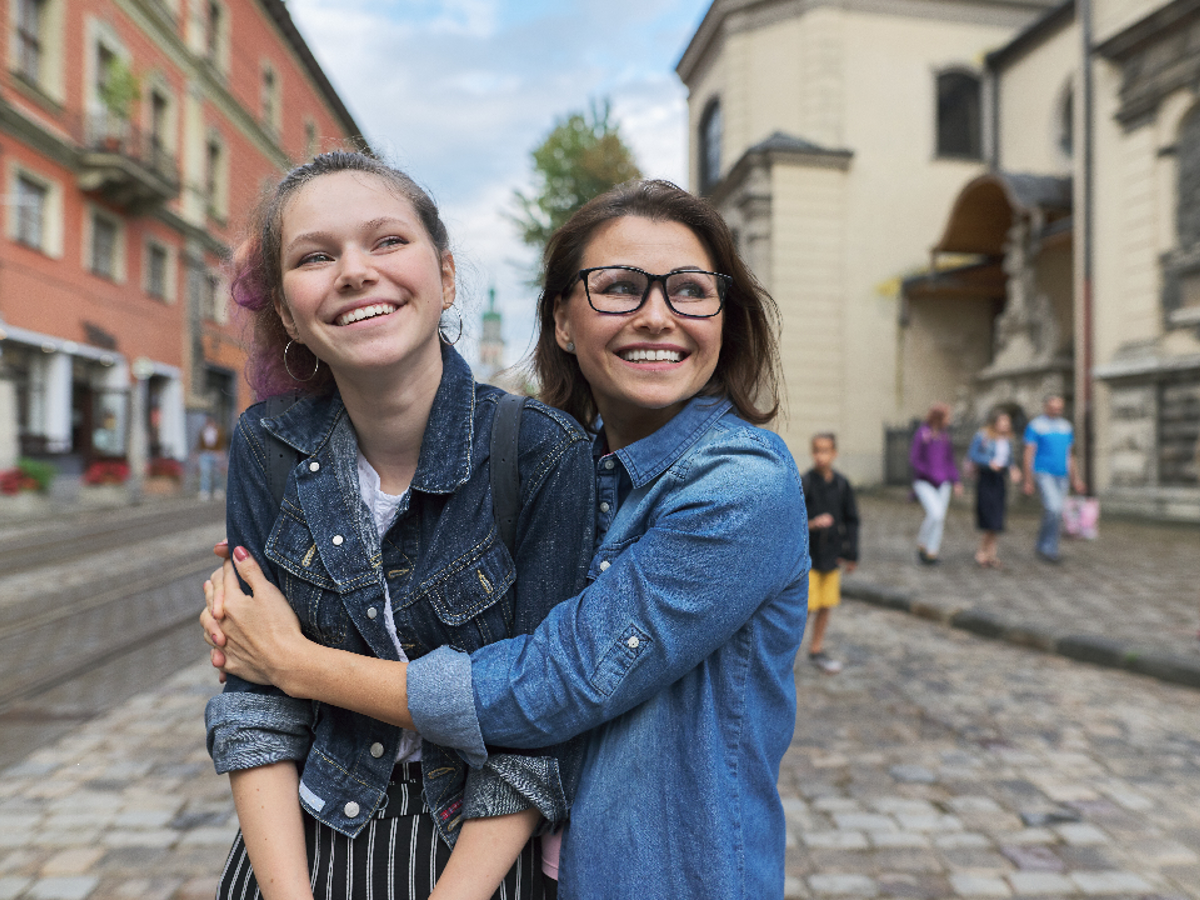 A teenage girl standing in the middle of a city being hugged sideways by another teenage girl