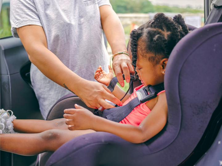 Child being clipped into a car seat by an adult
