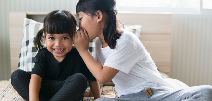 girl whispering into ear of laughing friend
