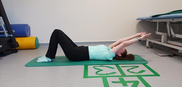 Child laying face up on a yoga mat with legs bent and arms raised straight above her head pointing behind her. 