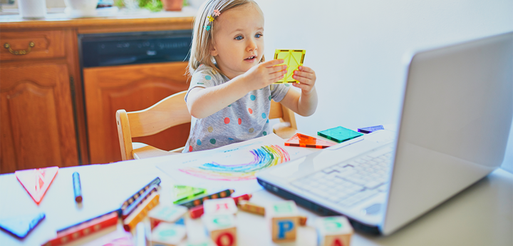 Toddler girl sitting on a chair at kitchen table and playing with colourful shapes