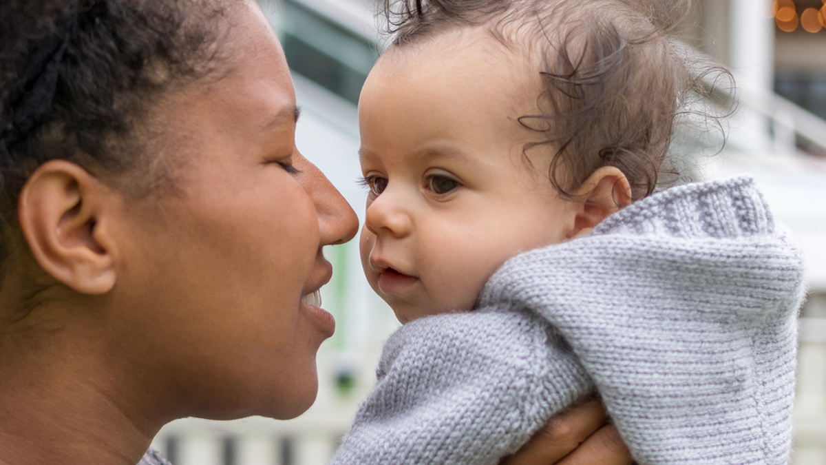 Mum holding baby boy up to her face smiling with her eyes shut.