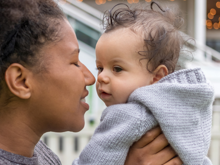 Mum holding baby boy up to her face smiling with her eyes shut.