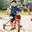 Boy sitting on tricycle with red and yellow car in background