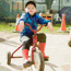 Boy sitting on tricycle with red and yellow car in background