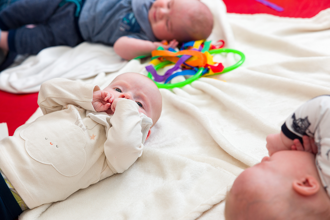 3 young babies lying on their backs on a white blanket 