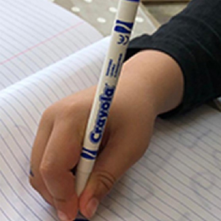 Child demonstrating the static tripod grasp with a blue crayon onto lined white paper