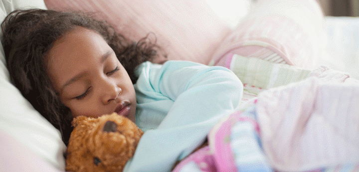 Young girl asleep in bed cuddling a teddy bear