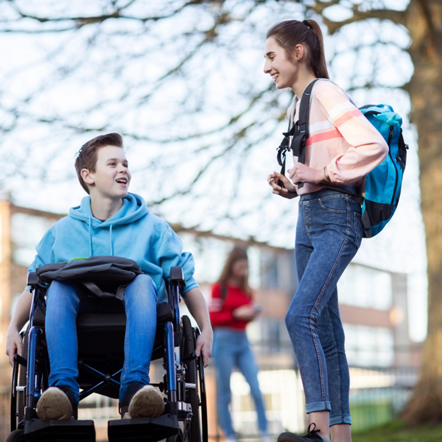 Teenage boy in wheelchair talking to a teenage girl outside their high school
