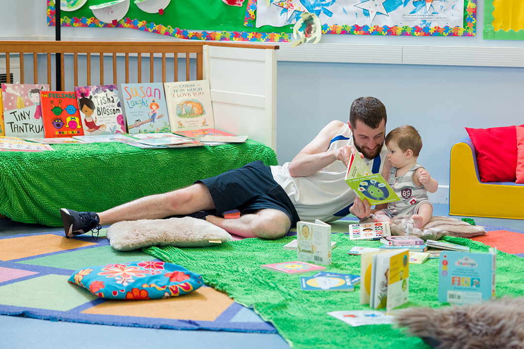 dad and toddler reading a book on the floor in a library