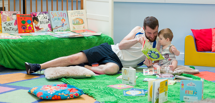 dad and toddler reading a book on the floor in a library
