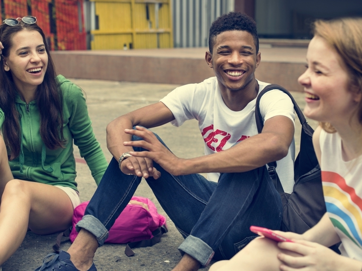 Three teenagers sitting on the ground laughing with each other