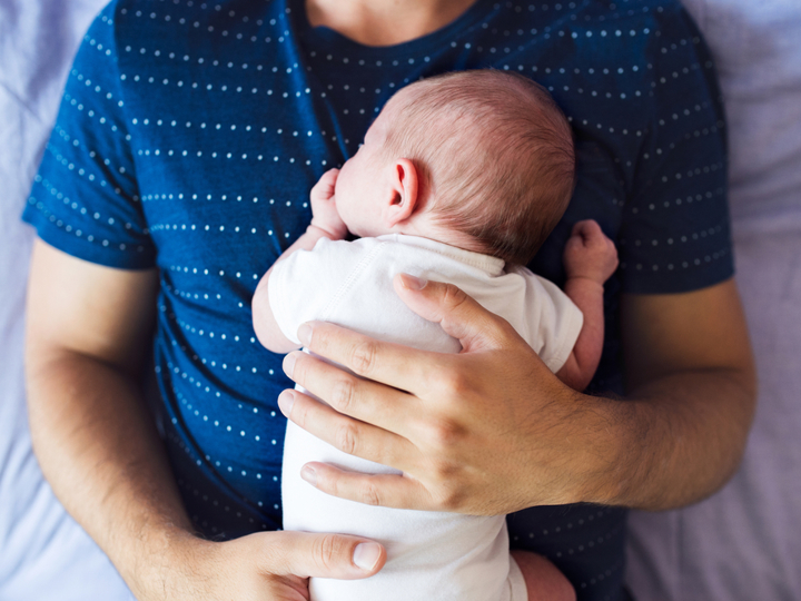 Young baby lying face down on a man's stomach