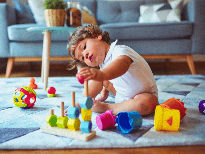 Toddler sitting on the floor in a sitting room, playing with toys on the carpet.