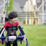 Young boy outside smiling being supported to walk by a walking aid.