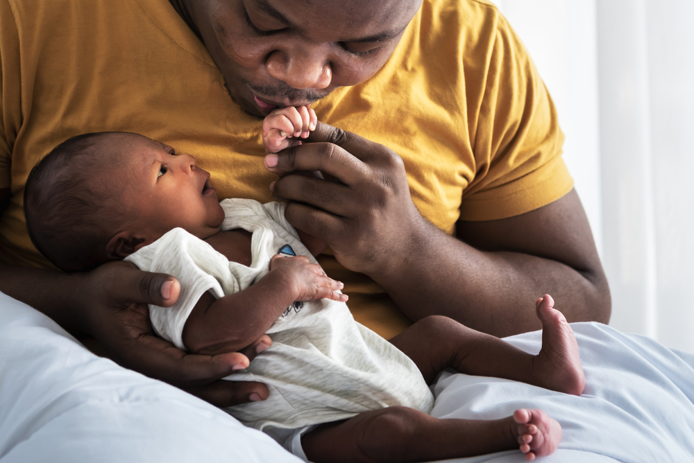 A dad holding a newborn baby in his arms and kissing their hand