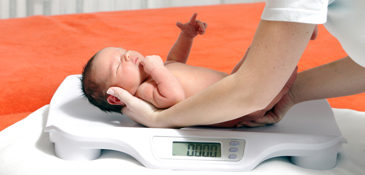 Naked new-born baby being laid on scales by an adult.
