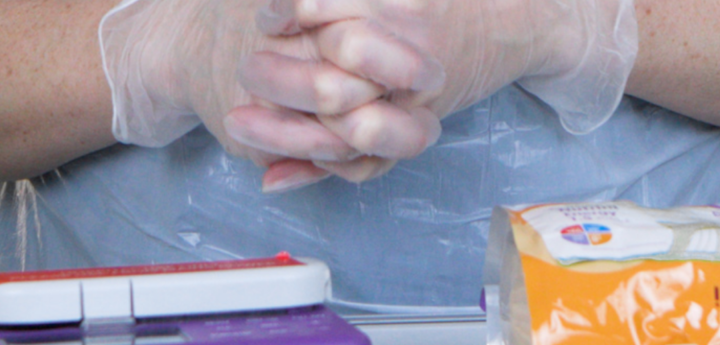 Adult clasping their hands with surgical gloves on behind a table with feeding equipment