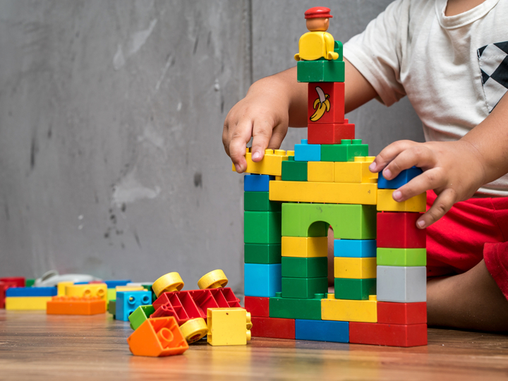 Young toddler sitting on the floor building a house from plastic blocks. 